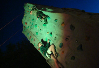 Twee kinderen beklimmen 's nachts een verlichte klimwand op Camping Seasonova Le Point du Jour in Normandië, Frankrijk.