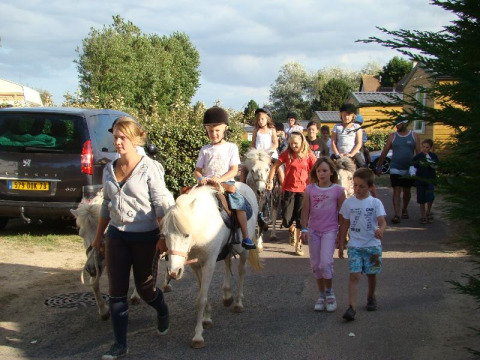 Niños montando ponis acompañados por adultos en Camping Seasonova Le Point du Jour, Normandía, Francia.