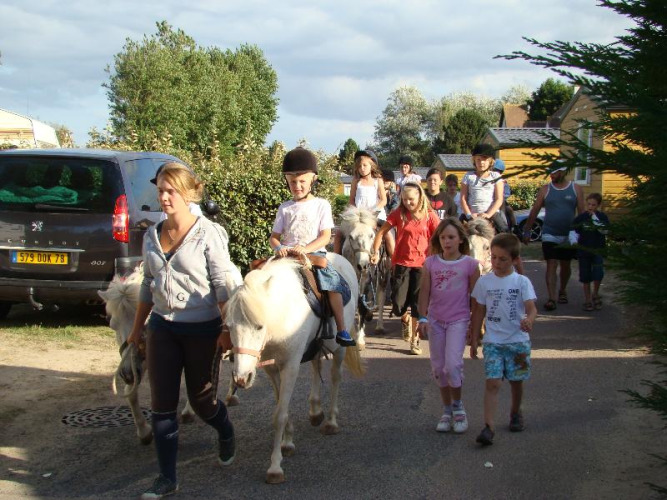 Kinder reiten auf Ponys, begleitet von Erwachsenen, im Camping Seasonova Le Point du Jour in der Normandie.