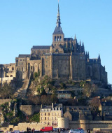 Photo de l’abbaye du Mont Saint-Michel perchée sur un rocher en Normandie, France, sous un ciel bleu.
