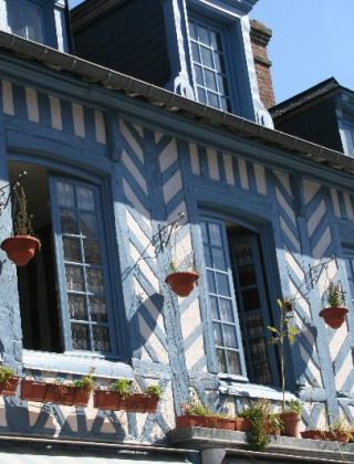 Maison à colombages bleus et blancs avec fenêtres ouvertes et pots de fleurs à Merville Franceville Plage.