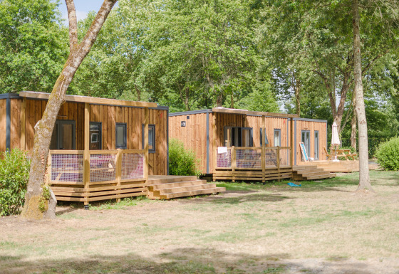 Holzhütten der Prestige Cottage Lodge, umgeben von Bäumen und grüner Natur an einem sonnigen Tag.