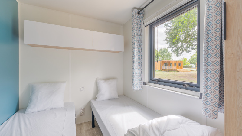 Kamer in Prestige Cottage met twee eenpersoonsbedden, groot raam, lichte gordijnen en uitzicht buiten.