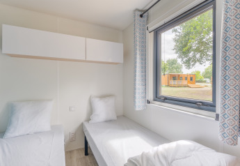 Chambre au Prestige Cottage avec deux lits simples, grande fenêtre, rideaux à motifs et vue sur la nature.