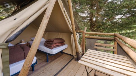 Vista da una tenda safari con due letti singoli e terrazza in legno immersa tra alberi verdi.