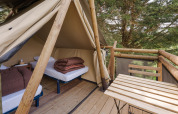 View from a safari tent with two single beds and a wooden terrace overlooking lush green trees.