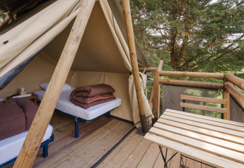 View from a safari tent with two single beds and a wooden terrace overlooking lush green trees.