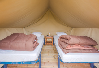 Interieur van een safaritent met twee losse bedden, bruine dekbedden en een kastje ertussen op houtenvloer.