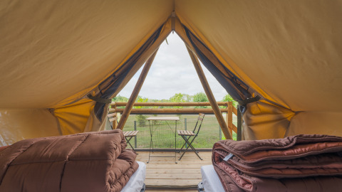 Vista dall'interno di una tenda safari con letti, coperte e terrazza con tavolo e sedie su prato.
