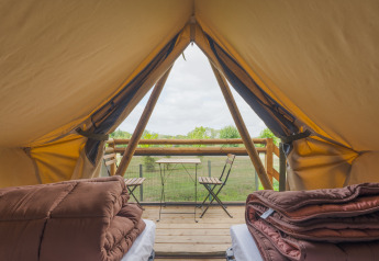 Vista dall'interno di una tenda safari con letti, coperte e terrazza con tavolo e sedie su prato.