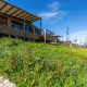 Træhytter på skråning med vilde blomster, blå himmel og grønne marker ved Cottage Premium Lodge.