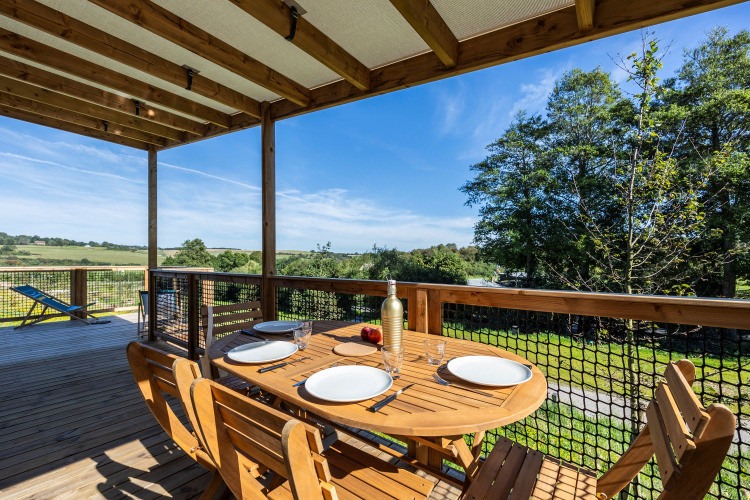 Wooden terrace with a set dining table overlooking greenery at Cottage Premium, Domaine Seasonova Saâne et Mer, France.
