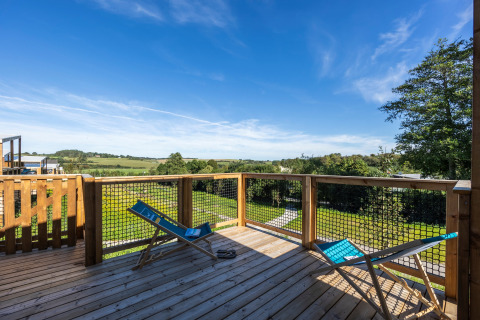 Terraza de madera con dos tumbonas azules y vistas a campos verdes en Domaine Seasonova Saâne et Mer, Francia.
