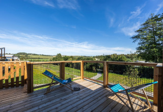 Holzterrasse mit zwei blauen Liegestühlen und weitem Blick ins Grüne im Cottage Premium, Frankreich.