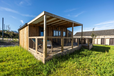 Prestige Cottage lodge met houten buitenkant, overdekt terras en grasveld onder een heldere blauwe lucht.