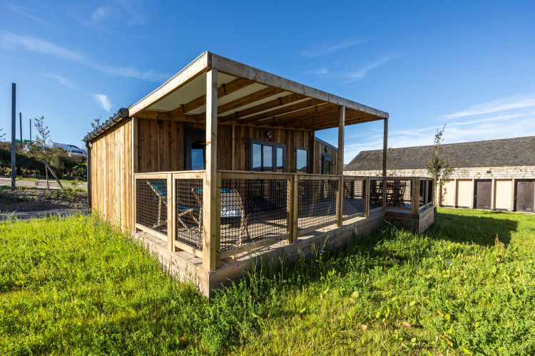 Cabaña Prestige Cottage con fachada de madera, terraza techada y césped bajo un cielo azul despejado.