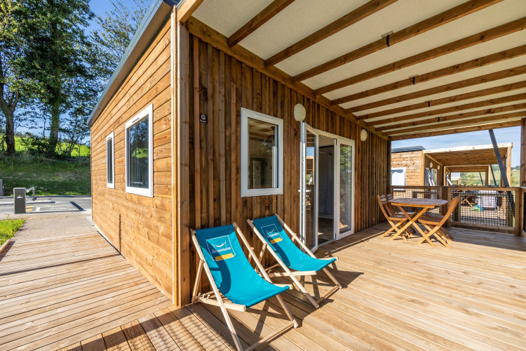 Accessible Cottage PMR lodge with a spacious wooden deck, lounge chairs, and outdoor dining area under roof.