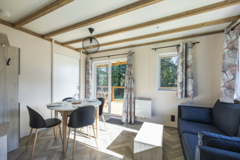 Lyst interiør af et tilgængeligt sommerhus med spisebord, stole, sofa og store vinduer på Domaine Seasonova.
