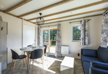 Lyst interiør af et tilgængeligt sommerhus med spisebord, stole, sofa og store vinduer på Domaine Seasonova.