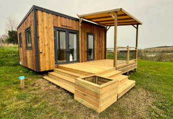 Træhytte ved navn Cottage med overdækket terrasse og trappe, omgivet af grønt græs og åben himmel.