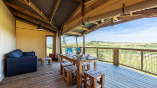 Overdækket terrasse af en safari telt Ecolodge med spisebord, sofa og udsigt over de åbne marker.