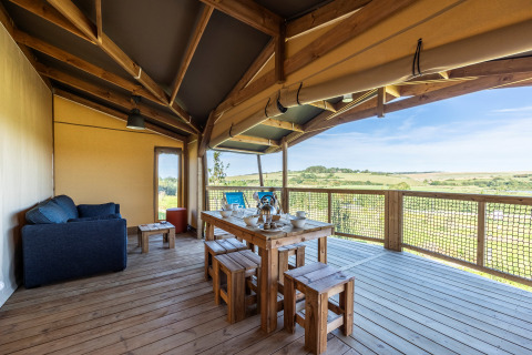 Terraza cubierta de una tienda safari Ecolodge con mesa de comedor, sofá y vistas al campo abierto.