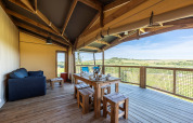 Terrasse couverte d’une tente safari Ecolodge avec table à manger, canapé et vue sur la campagne.