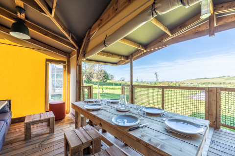 Zona de comedor en tienda safari Ecolodge con mesa de madera y vistas al campo verde luminoso.
