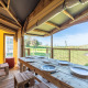 Spiseområde i Ecolodge safari-telt med træborde og udsigt over grønne marker og landskab.