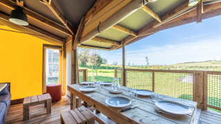 Zona de comedor en tienda safari Ecolodge con mesa de madera y vistas al campo verde luminoso.