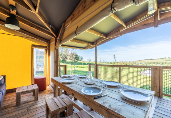 Spiseområde i Ecolodge safari-telt med træborde og udsigt over grønne marker og landskab.
