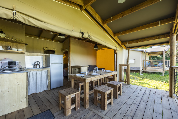 Interior de una tienda ecológica safari con cocina, mesa de comedor y terraza en Domaine Seasonova Saâne et Mer, Francia.