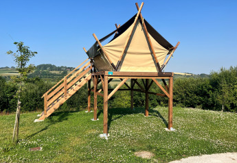 Tienda safari elevada sobre campo de césped, con escaleras de madera y cielo azul despejado.