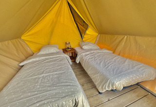 Two single beds with bedding inside a spacious glamping tent on wooden floor, lantern on nightstand.