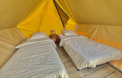 Deux lits simples avec couette dans une grande tente de glamping sur plancher en bois, lanterne au centre.