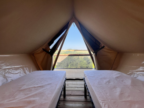 Interior of a safari tent with two beds and a beautiful scenic view outside the tent opening.