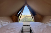 Interieur van een safaritent met twee bedden en prachtig zicht op het landschap bij de ingang.