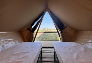 Interior of a safari tent with two beds and a beautiful scenic view outside the tent opening.