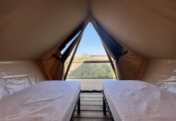 Innenansicht eines Safarizeltes mit zwei Betten und Ausblick auf die Landschaft durch den Eingang.