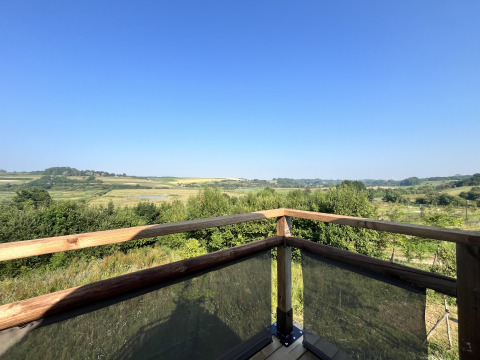 View from a safari tent deck with wooden railing overlooking green fields, hills, and a clear blue sky.