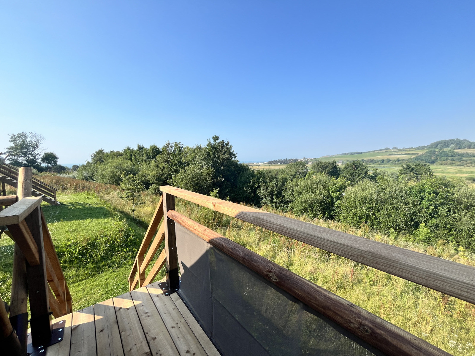 Uitzicht vanaf het terras van een safaritent op groene velden en bomen onder een heldere blauwe lucht.