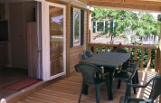Wooden patio with plastic chairs and table at Cottage Zen, Camping Seasonova La Forêt in France.