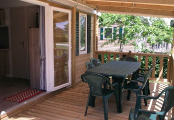 Wooden patio with plastic chairs and table at Cottage Zen, Camping Seasonova La Forêt in France.