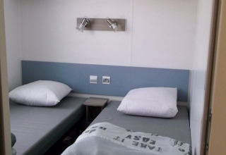 Dos camas individuales con ropa de cama gris en una pequeña habitación de Cottage Zen, Camping Seasonova La Forêt, Francia.