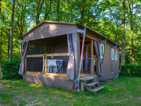 Tienda safari llamada Mobilodge ubicada en un bosque verde con terraza y mesa y sillas afuera.
