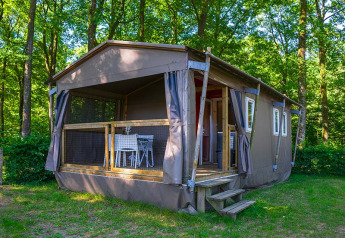 Safari tent called Mobilodge located in a green forest with a deck and outdoor table and chairs.
