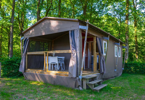 Safari tent called Mobilodge located in a green forest with a deck and outdoor table and chairs.
