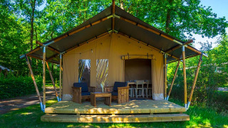 Tienda safari Slow Lodge con terraza de madera y muebles, rodeada de árboles verdes y naturaleza.