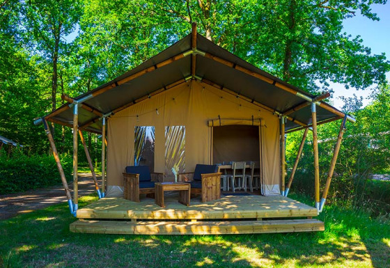 Tienda safari Slow Lodge con terraza de madera y muebles, rodeada de árboles verdes y naturaleza.