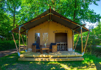 Safari-Zelt Slow Lodge mit Holzterrasse und Sitzgelegenheit im Freien, umgeben von grünen Bäumen.